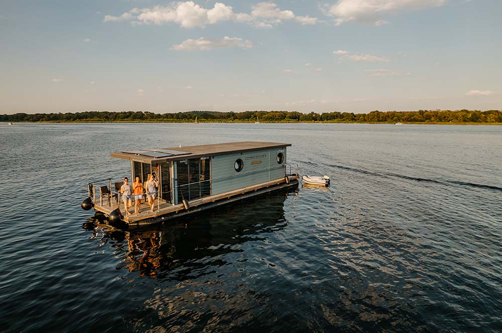 Freunde genießen das Wetter auf einem Hausboot in den ruhigen Gewässern Brandenburgs, perfekt für einen entspannten Urlaub.